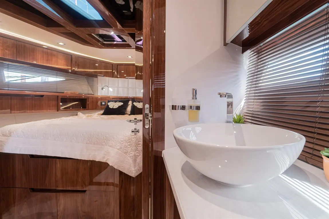 Luxurious yacht interior featuring a double bed, basin, and decorative plants, with wooden finishes and natural light.
